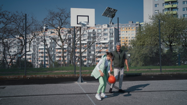 A happy father and teen daughter playing basketball outside at court.