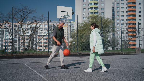 A happy father and teen daughter playing basketball outside at court.