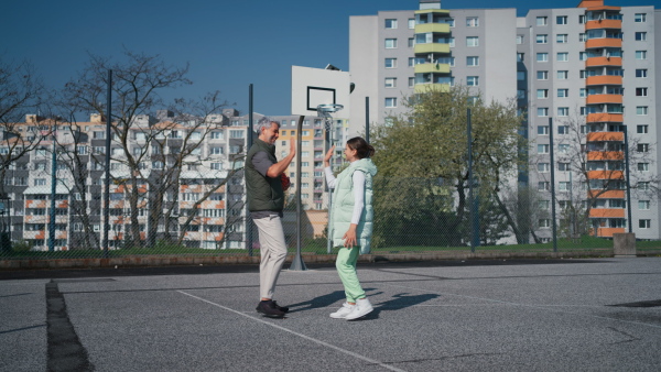 A happy father and teenage daughter high fiving after playing basketball outside at court.