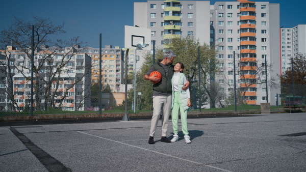 A happy father and teenage daughter high fiving after playing basketball outside at court.