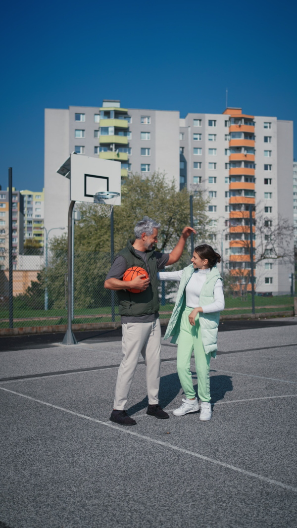 A vertical footage of happy father and teenage daughter high fiving after playing basketball outside at court.