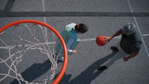 A father and teenage daughter playing basketball outside at court, high angle view above hoop net.