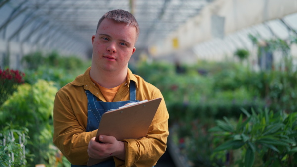 A young man with Down syndrome working in garden centre, holidng clipboard and checking plants.