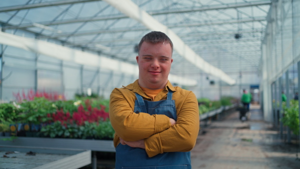 A young employee with Down syndrome working in garden centre, looking at camera with arms crossed.