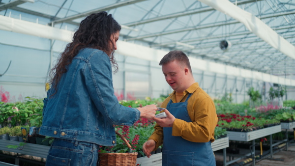 A happy young employee with Down syndrome working in garden centre, taking payment from customer.