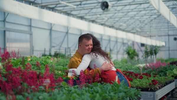 A woman florist hugging her young colleague with Down syndrome in garden centre.