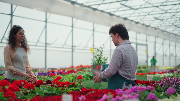 An experienced woman florist helping young employee with Down syndrome in garden centre.