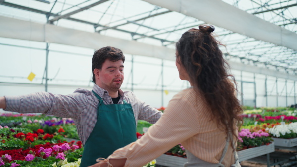 An experienced woman florist helping young employee with Down syndrome in garden centre.