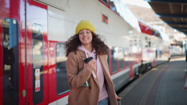 A happy young traveler woman with luggage running to catch the train at train station platform