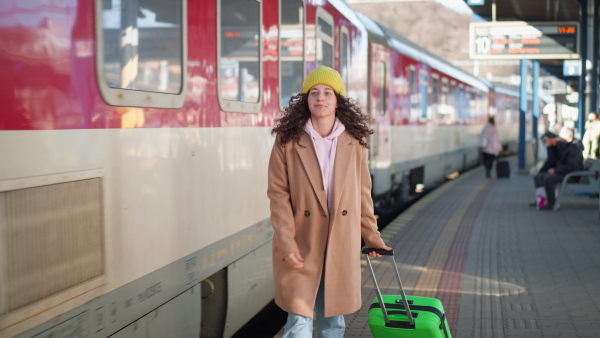 A happy young traveler woman with luggage and cup of coffee boarding in the train at train station platform