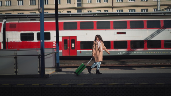 A happy young traveler woman with luggage and cup of coffee boarding in the train at train station platform