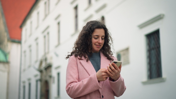 A happy young commuter woman using mobile phone whan walking in street in autumn.