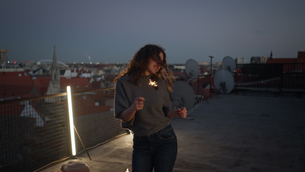 A young woman with sparklers having fun at rooftop in the city, close up.