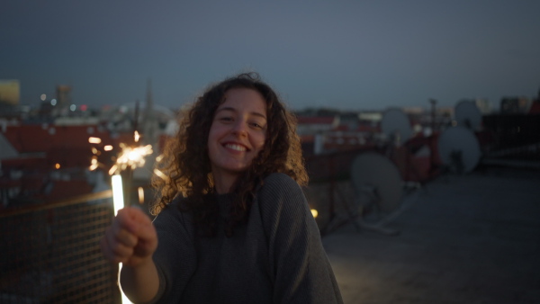 A young woman with sparklers having fun at rooftop in the city, close up.