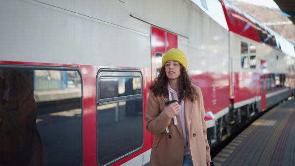 A portrait of happy young traveler woman with coffe and luggage at train station platform