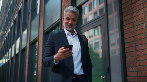 A successful happy businessman walking in city street, calling on mobile phone, commuting concept.