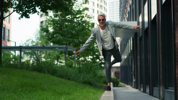 A fun portrait of happy energetic mature businessman with arms outstretched balancing on wall , feeling free, work life balance concept.