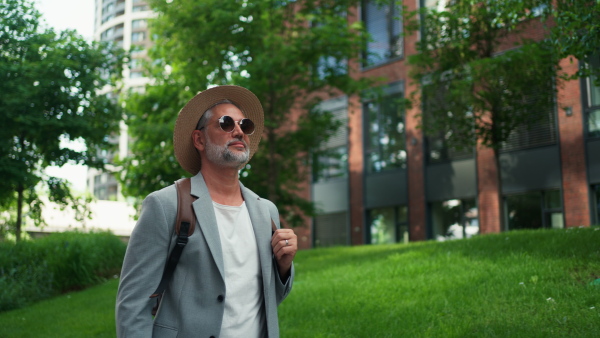 A confident man wearing straw hat and backpack walking in street, businessman in casual clothes in summer on the way to work.