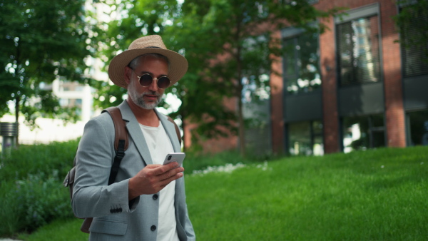 A confident man wearing straw hat and backpack using phone, businessman in casual clothes in summer on the way to work.