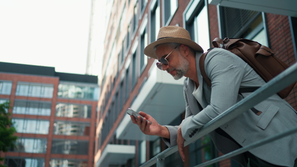 A confident man wearing straw hat and backpack using phone, businessman in casual clothes in summer on the way to work.