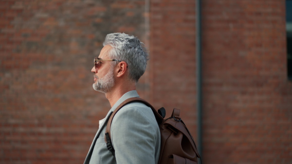 A confident man wearing backpack walking in street, businessman in casual clothes in summer on the way to work.