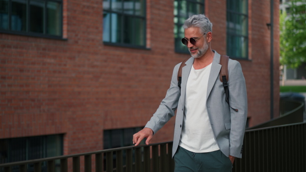 A confident man withd backpack walking in street, businessman in casual clothes in summer on the way to work.