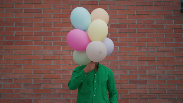 A fun portrait of happy energetic mature man holding balloons in street , feeling free.