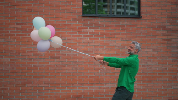 A fun portrait of happy energetic mature man holding balloons in street , feeling free.