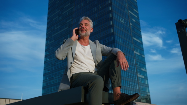 Confident businessman sitting on stairs and using phone, feeling free, escaping from work, work life balance concept.