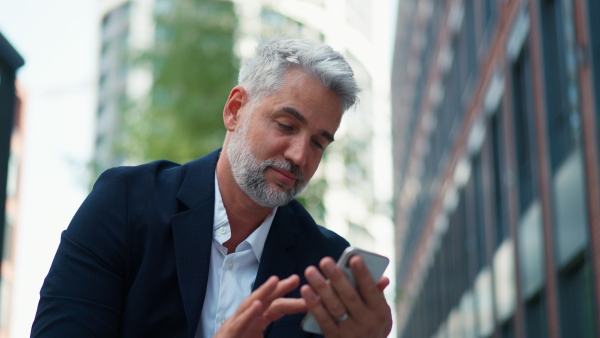 A successful happy businessman walking in city street, calling on mobile phone, commuting concept.