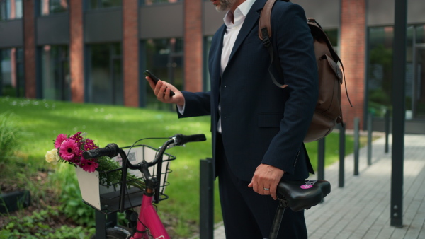 A businessman with bike and bouquet using smartphone. Commuting and alternative transport concept