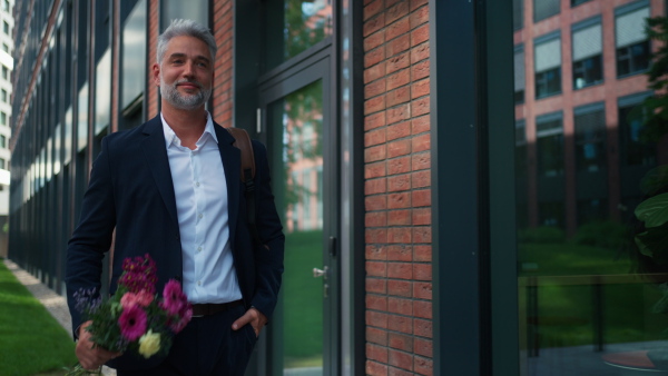 A happy mature businessman with flower bouquet walking in street to meet his girlfriend.