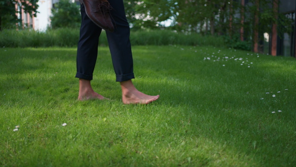 A businessman carrying shoes and walking barefoot in park, feeling free, work life balance concept, close-up