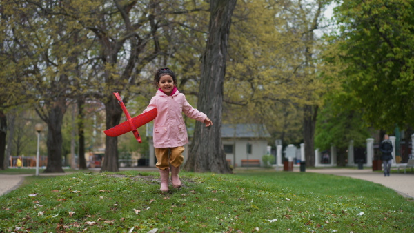 Happy girl running in park with airplane toy, looking into camera.