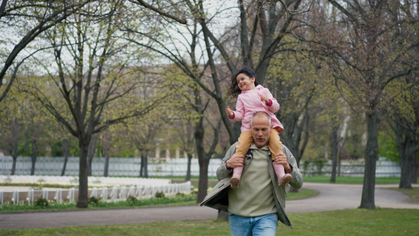 Mature father and little daughter in park. Father carrying joyful girl on shoulders, having fun together.