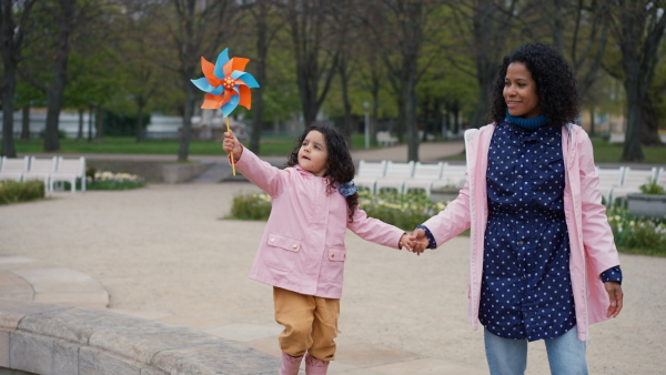 Mother and little daughter walking in park. Girl holding a toy windmill.