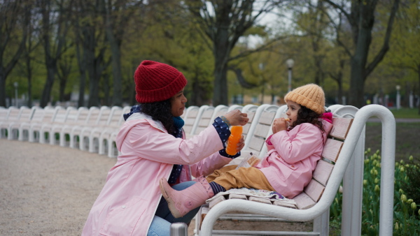 Mother with small daughter on park bench having a afternoon snack.