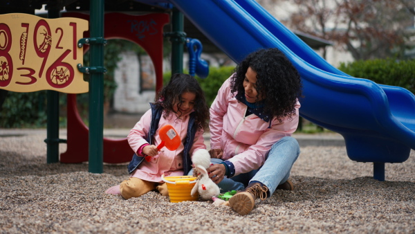 Mother playing with little daughter on playground with sand moulds and bucket.