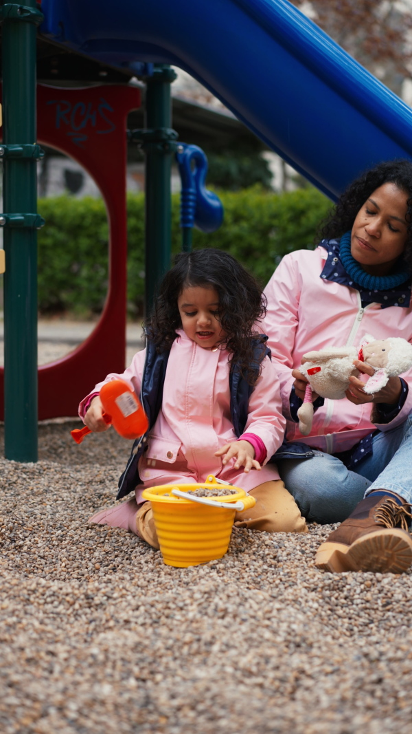 Mother playing with little daughter on playground with sand moulds and bucket. Vertical shot.