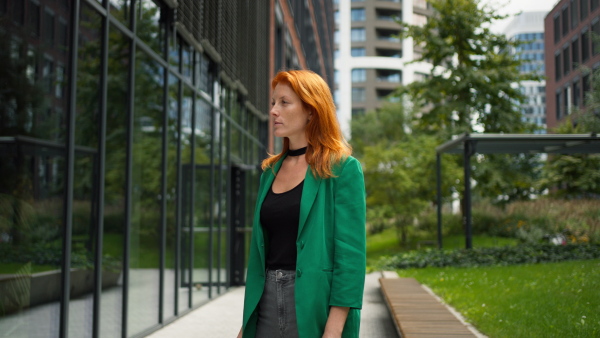 Young stylish redhead woman standing in a city and posing.