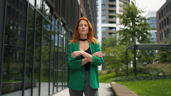 Young stylish redhead woman standing in a city and posing.