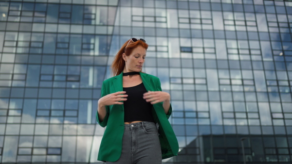 Young stylish redhead woman standing in a city and posing.