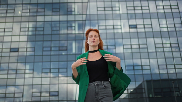 Young stylish redhead woman standing in a city and posing.