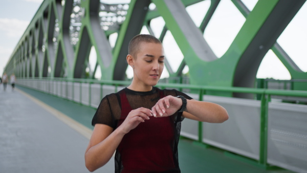 Young sportive woman checking her smartwatch after jogging in a city.