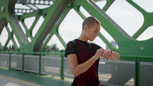 Young sportive woman checking her smartwatch after jogging in a city.