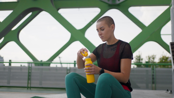 Young sportive woman drinking water and resting after morning run in a city.