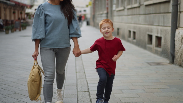 Youg mother with her little redhead son walking in a city.