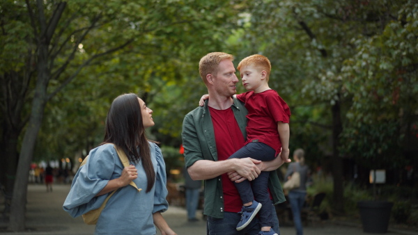 Young family with their son in a city park, father carrying him in arms.