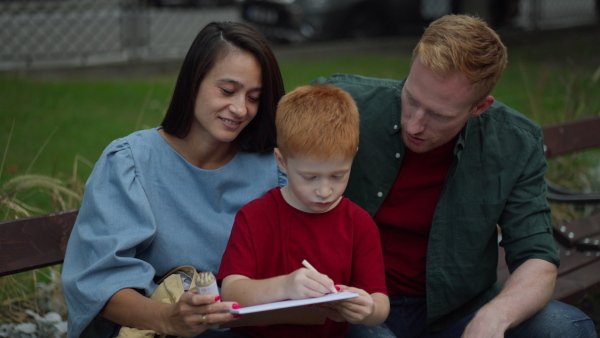 Little redhead boy drawing with his parents, outdoor in a city park.