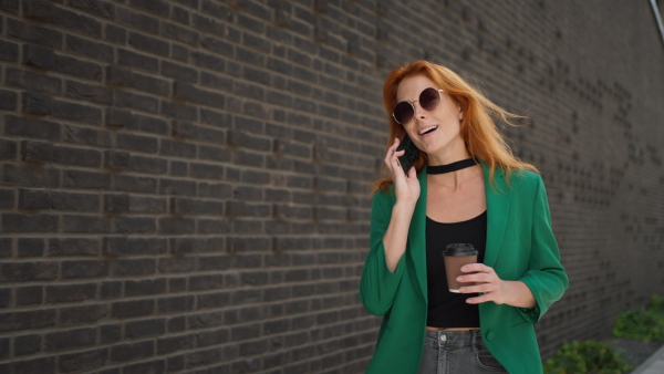 Young woman calling and walking in the city with a cup of coffee.